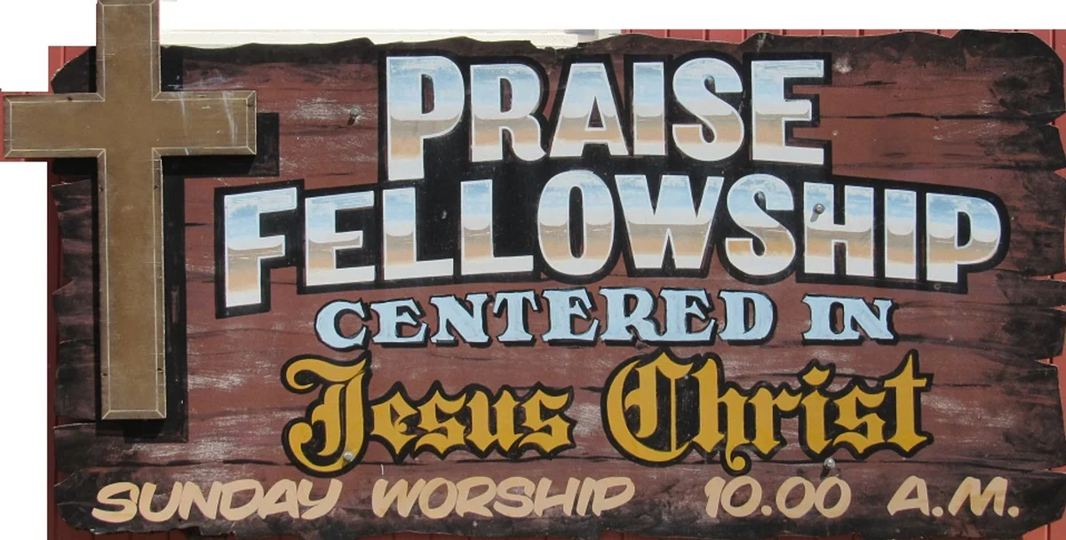 Hand-painted Praise Fellowship sign with a cross: Centered in Jesus Christ. Sunday worship 10:00 A.M.